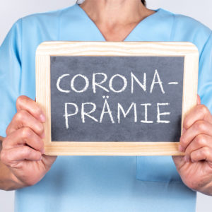Person hält Schild mit Aufschrift Corona-Prämie