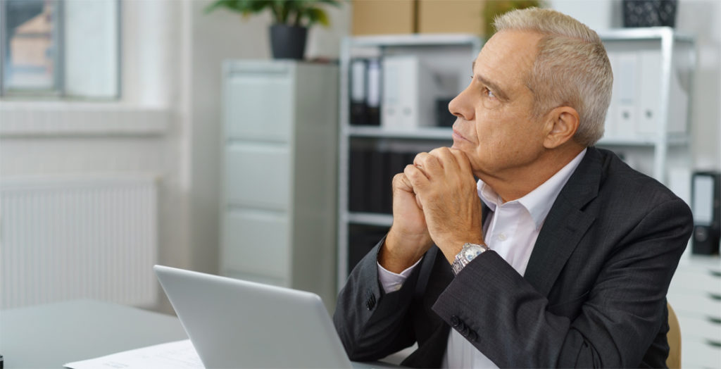 Älterer Arbeitnehmer vor Laptop schaut nachdenklich in die Ferne