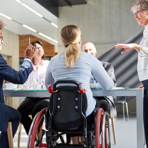 Geschäftsleute im Meeting mit Kollegin im Rollstuhl.