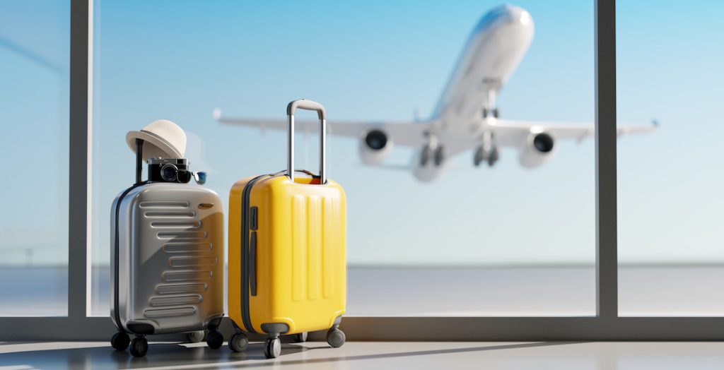 Koffer an einem Flughafen mit startendem Flugzeug im Hintergrund