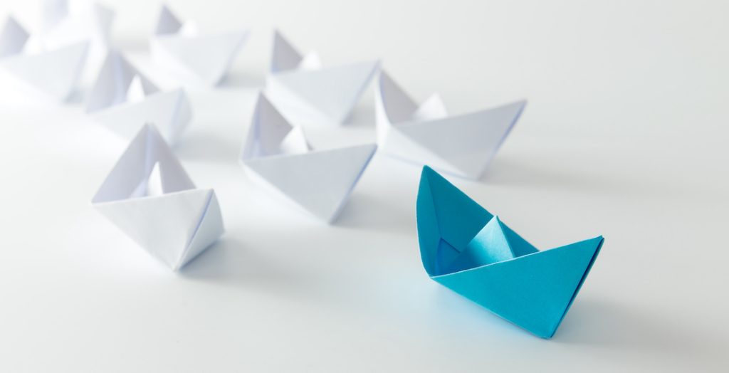 Ein blaues Papierschiff leitet andere