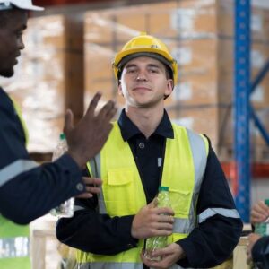 Beschäftigte in Warnwesten unterhalten sich in einer Lagerhalle.